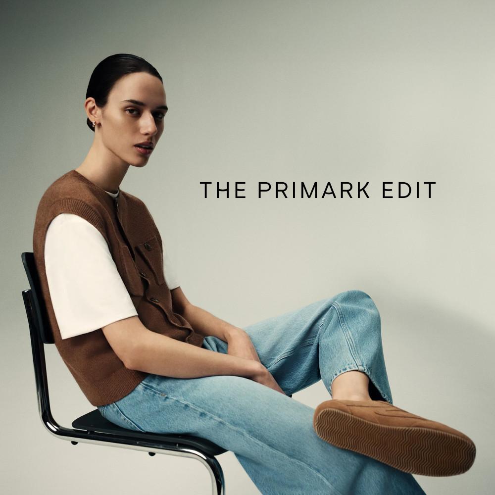 Persona con chaleco de punto marrón sobre una camiseta blanca y vaqueros azul claro, sentada en una silla. Texto «THE PRIMARK EDIT».