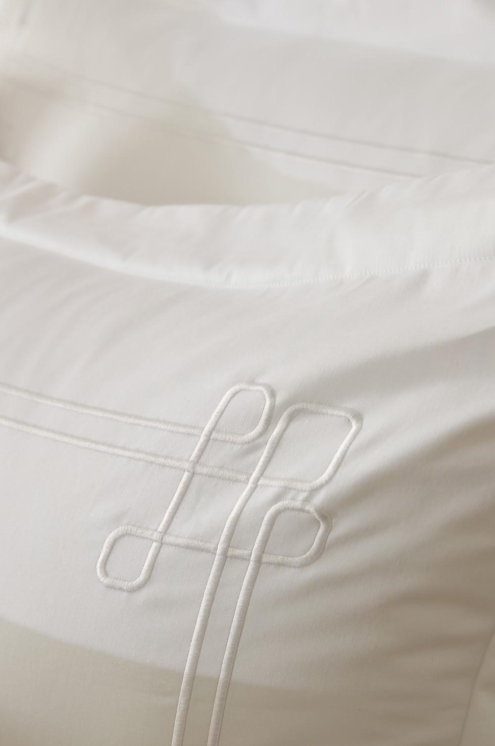 Primer plano de ropa de cama blanca con un monograma bordado como detalle decorativo.