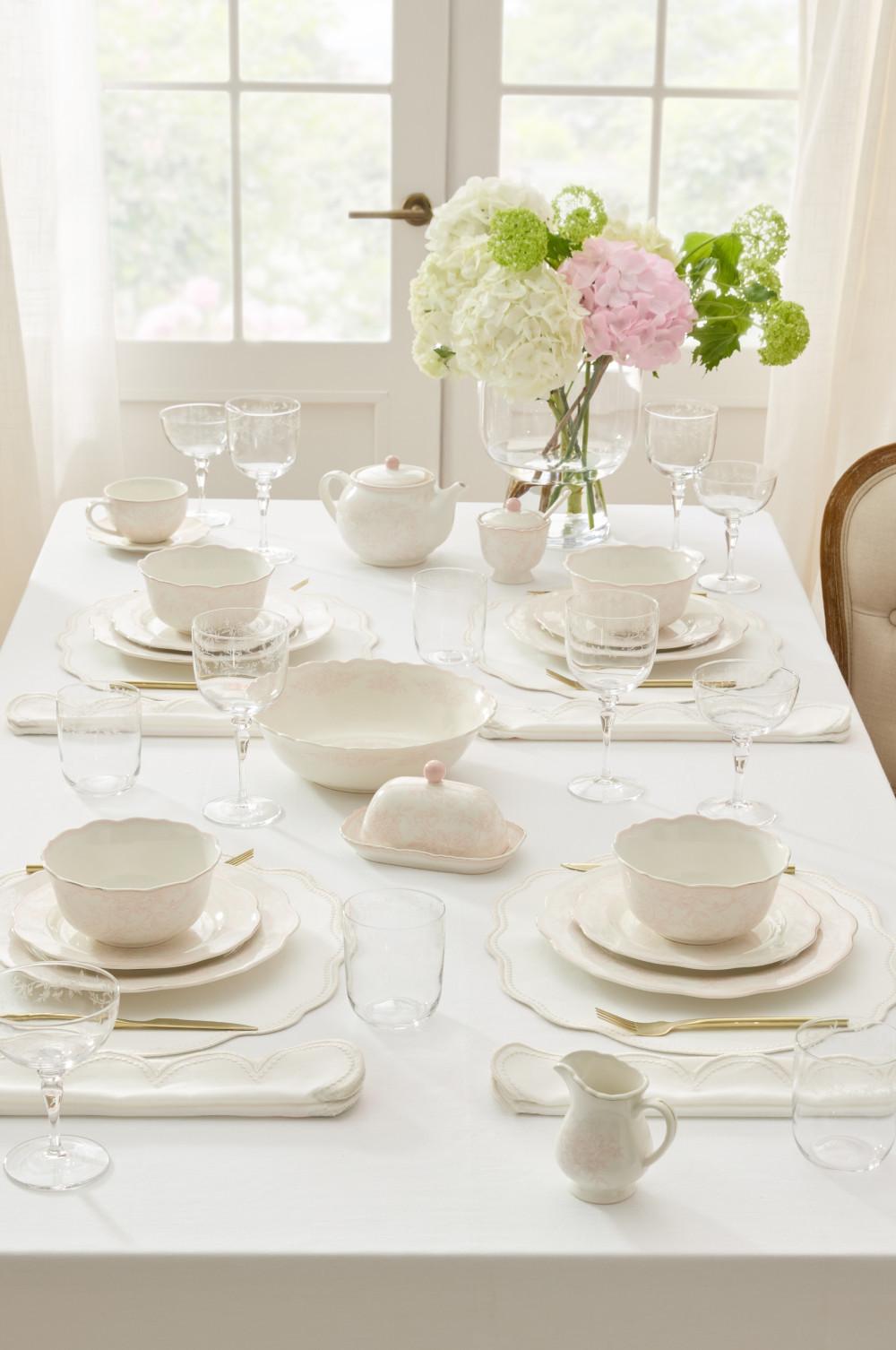 Elegante servicio de mesa blanco con vajilla de porcelana, cristalería y un centro floral de hortensias.