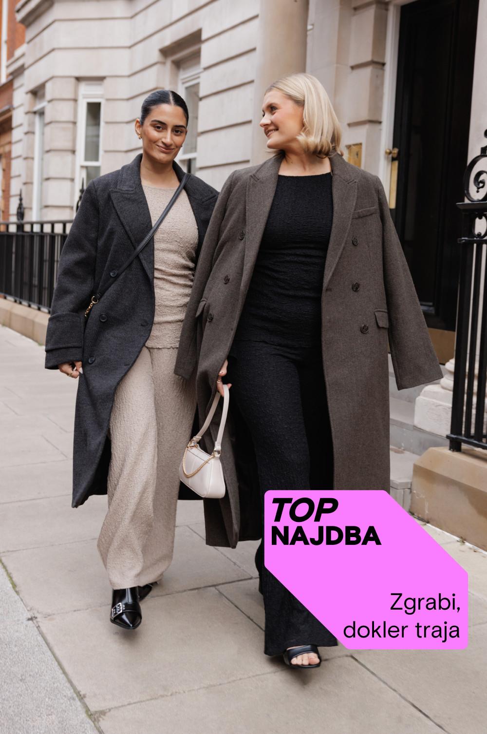 Dve ženski hodita skupaj v modnih zimskih plaščih in elegantnih opravah pred stavbo. Rožnata promocijska oznaka »MAJOR FIND«