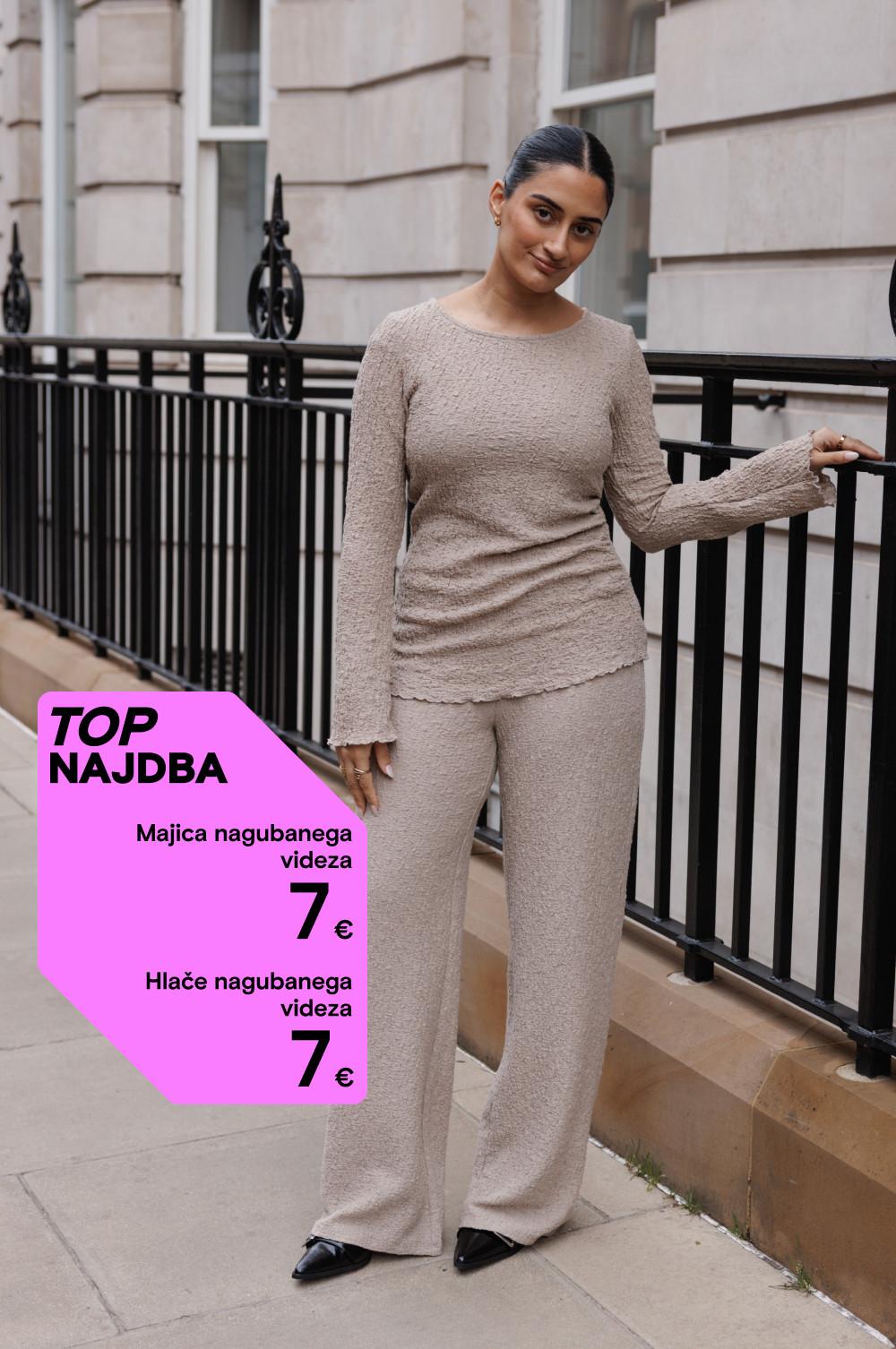 Komplet bež majice in hlač z zmečkano teksturo po ceni 7 € na kos, prikazan pred stavbo z železno ograjo.