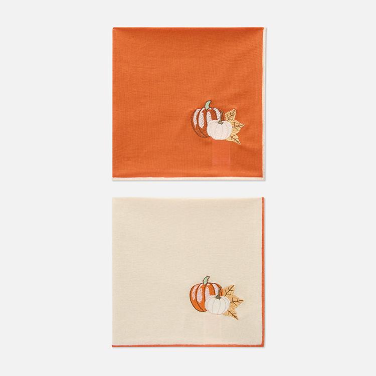 Two autumn napkins with embroidered pumpkin designs, one orange and one cream-coloured.