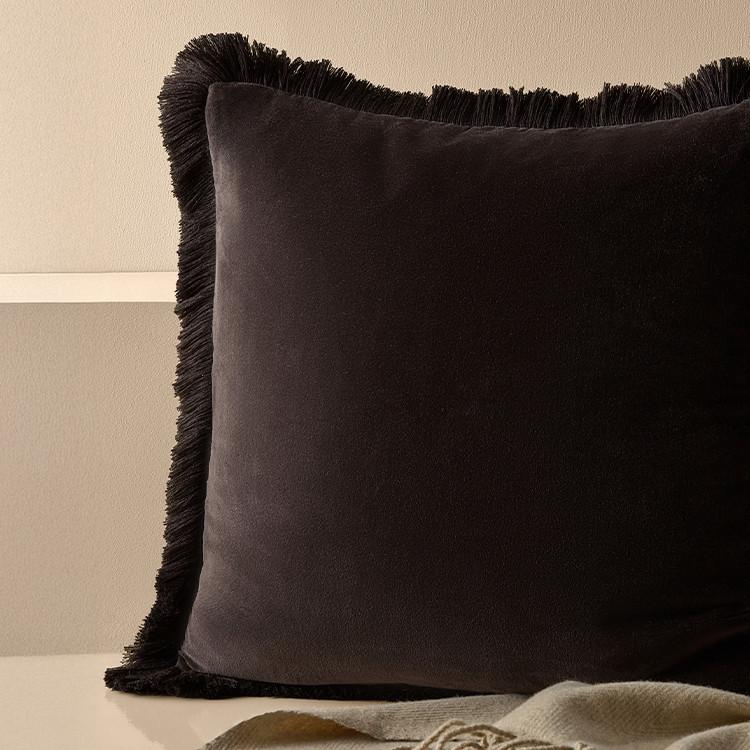 Dark brown decorative cushion with fringe trim edges against a neutral beige background.