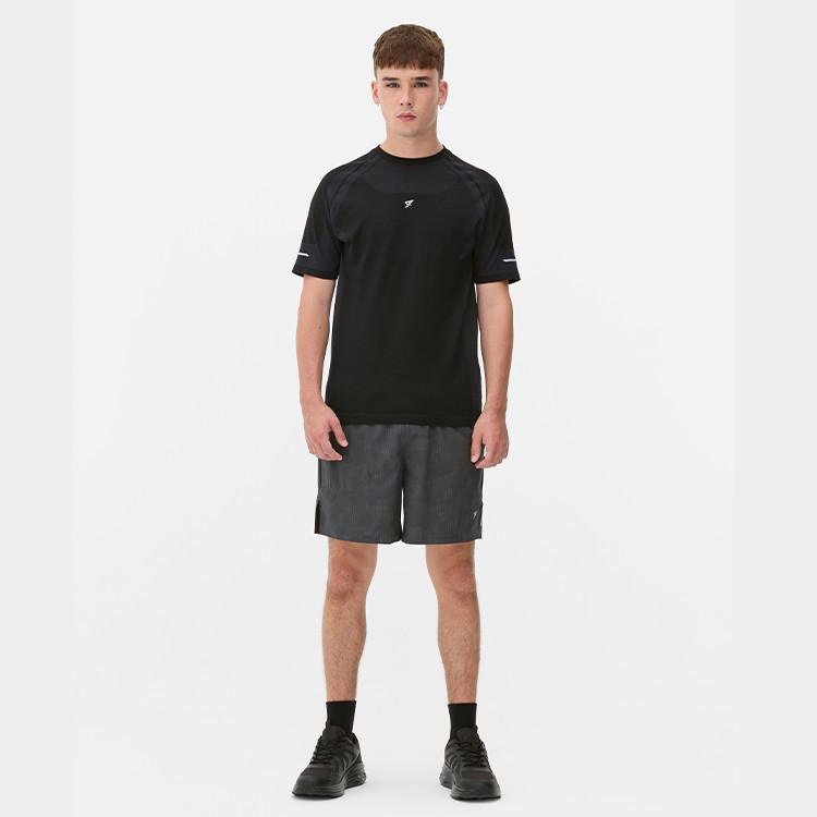 Person wearing black athletic t-shirt with small logo and grey shorts, standing against white background.