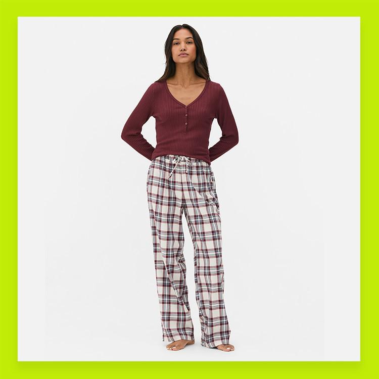Woman wearing burgundy ribbed henley top with plaid pyjama bottoms in white and red check pattern.