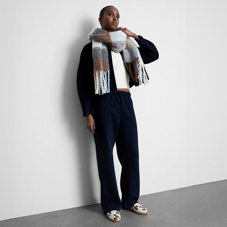 Person wearing navy outfit with white crop top and patterned scarf, posing against white wall.