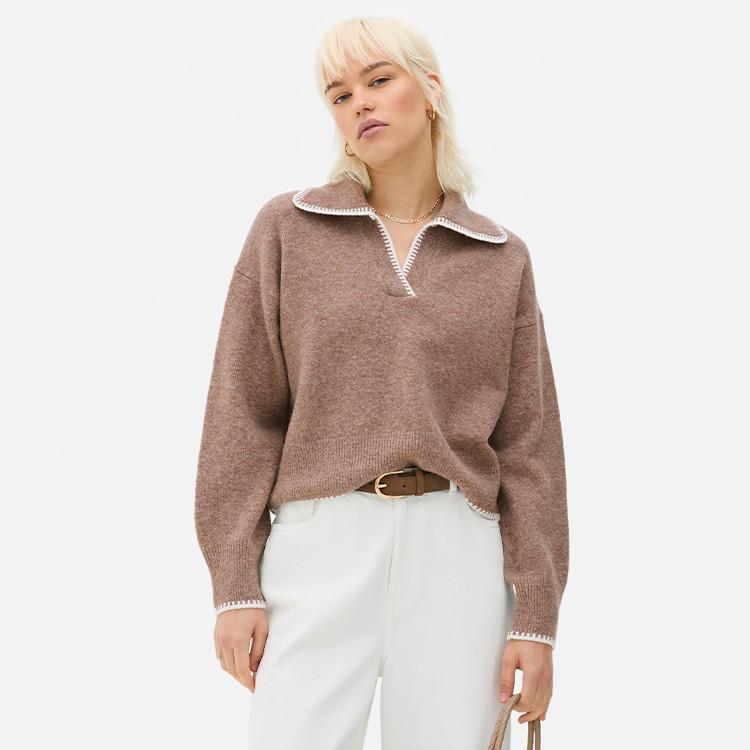 Person wearing brown collared sweater with white trim, paired with white trousers and brown belt.