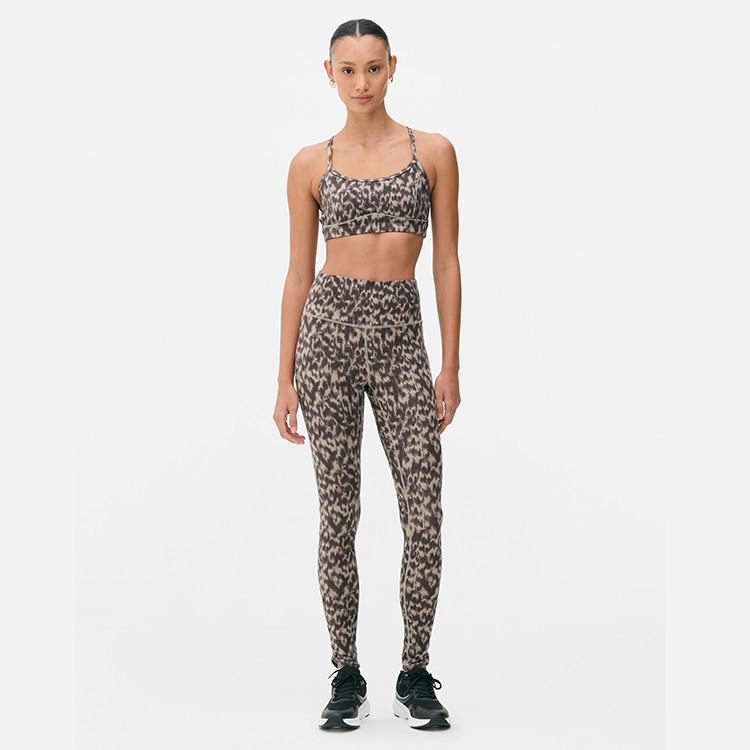 Woman wearing leopard print sports bra and matching leggings with black trainers.