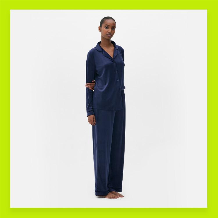 Model wearing navy blue satin pyjama set with button-up top and wide-leg trousers against white backdrop.