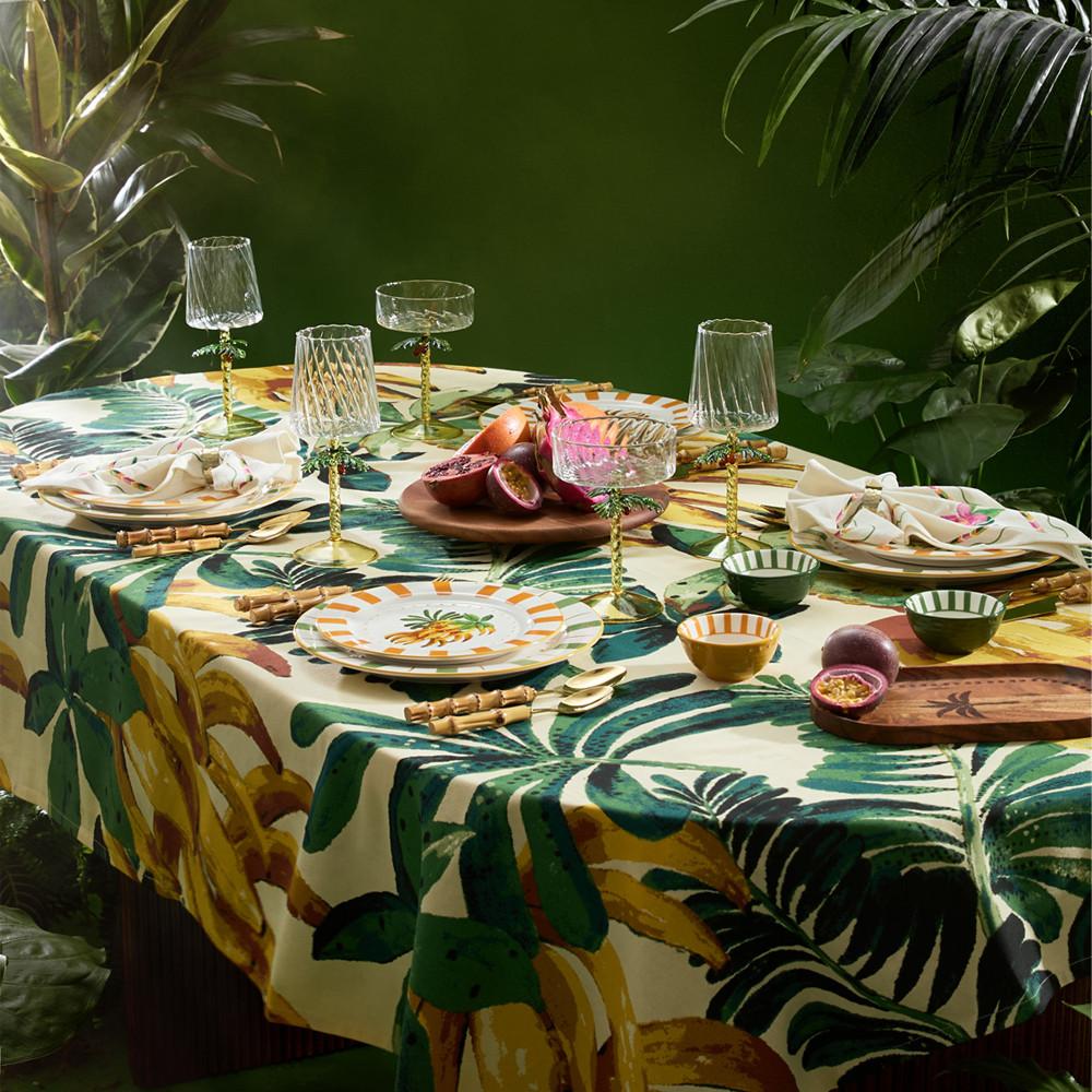 Family around a table having dinner outside with white bowls and tropical themed ceramics.