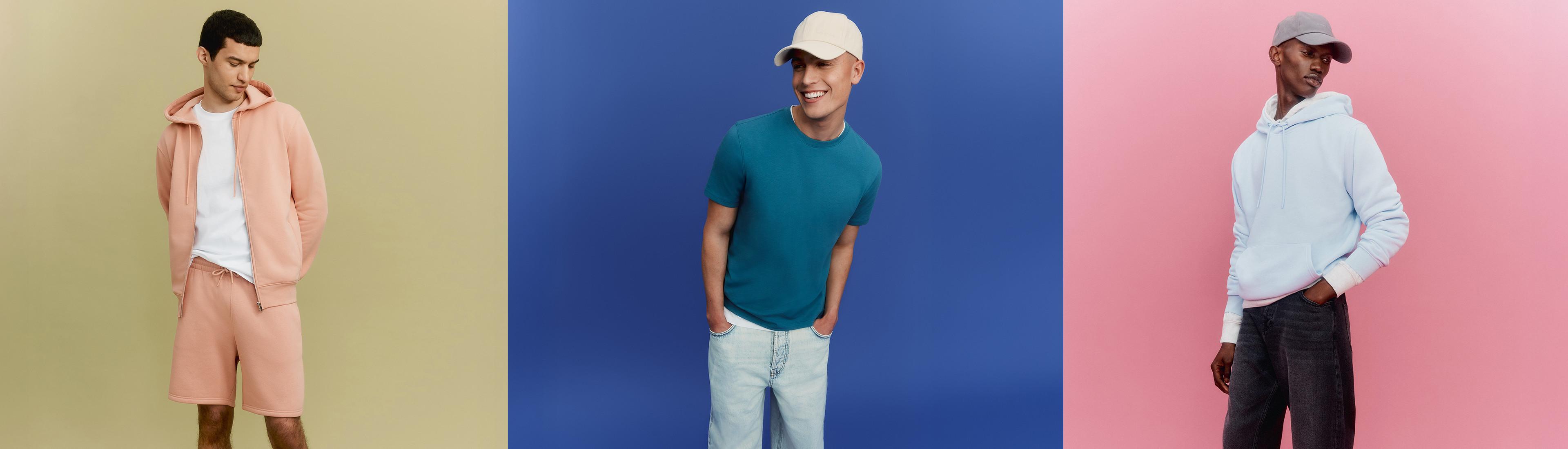 Drie mannen in casual outfits: een roze set van een hoodie met short, een groenblauw T-shirt met een lichte jeans en witte pet, en een witte hoodie met een donkere jeans en grijze pet.