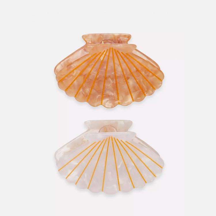 Two decorative seashell-shaped hair clips in pearlescent orange and white with gold ray patterns.