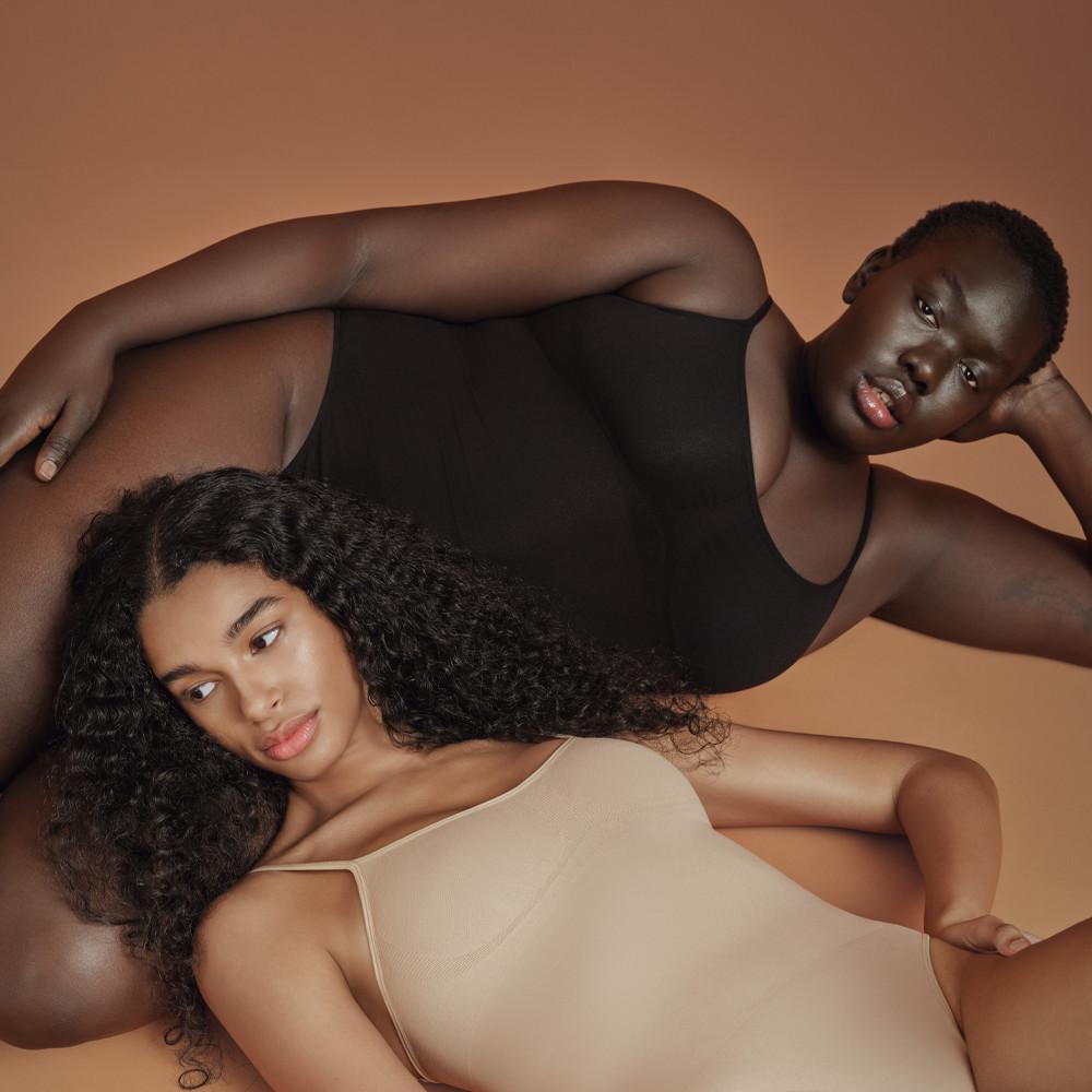 Zwei Models, die sich zurücklehnen, während sie nahtlose Bodys in schwarzen und nudefarbenen Tönen tragen.