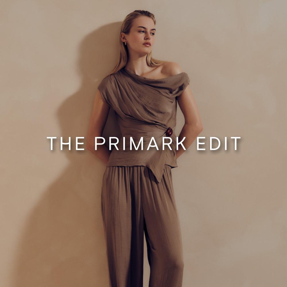 Eine Frau trägt ein taupefarbenes, schulterfreies, drapiertes Oberteil und eine dazu passende Hose mit weitem Bein aus der THE PRIMARK EDIT-Kollektion.
