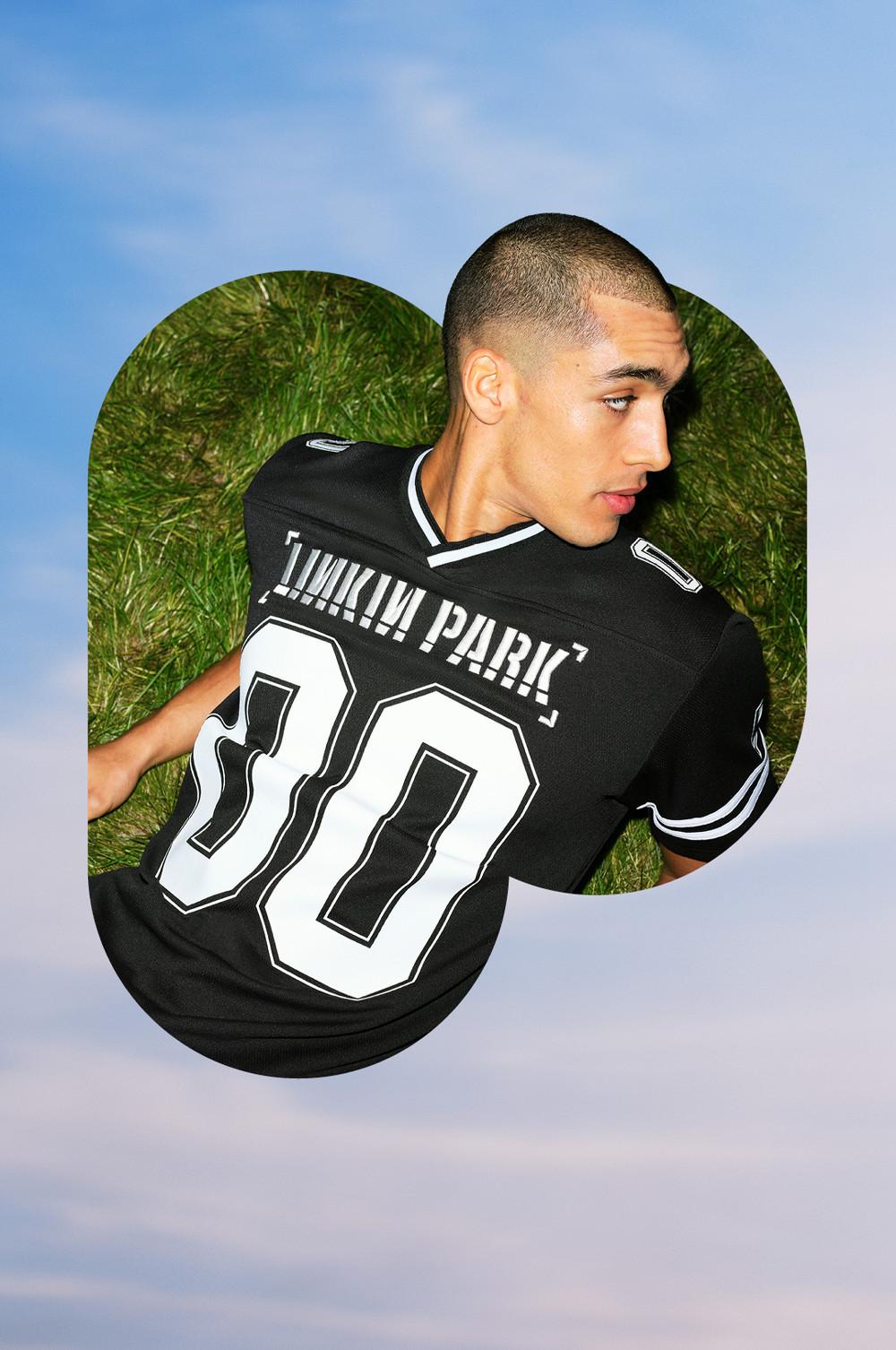 Male model wearing black Linkin Park number 30 sports jersey with white detailing lying on grass.