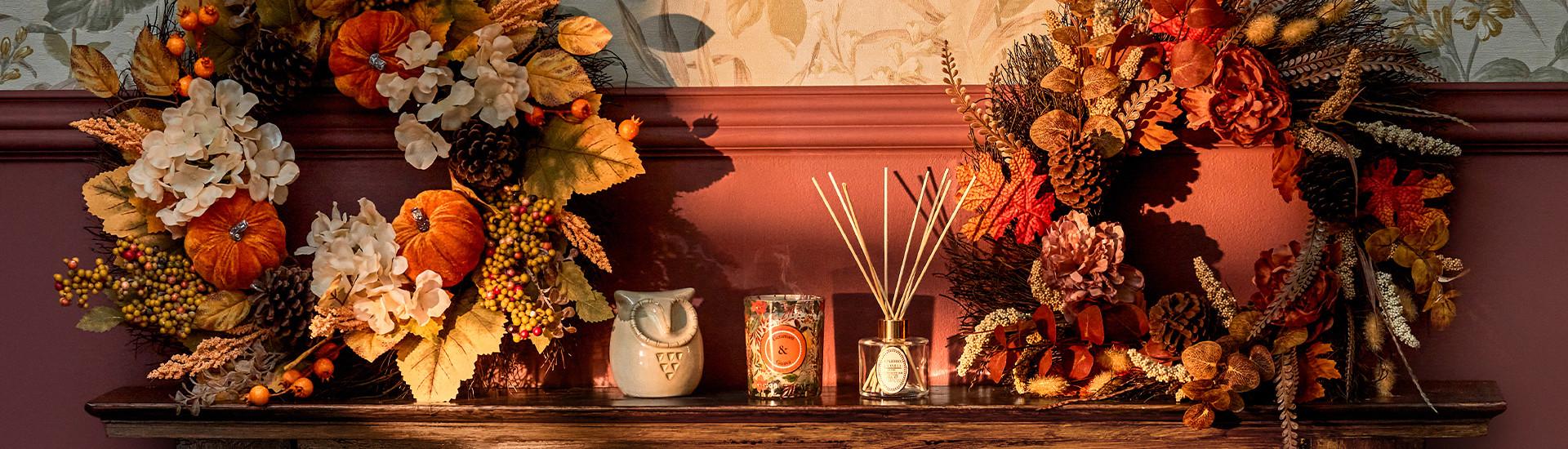Autumn display with decorative wreaths, small pumpkins, and home fragrance items on a wooden shelf.