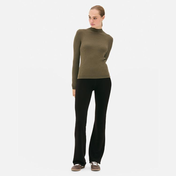 Olive green ribbed turtleneck jumper paired with black flared trousers and brown shoes.