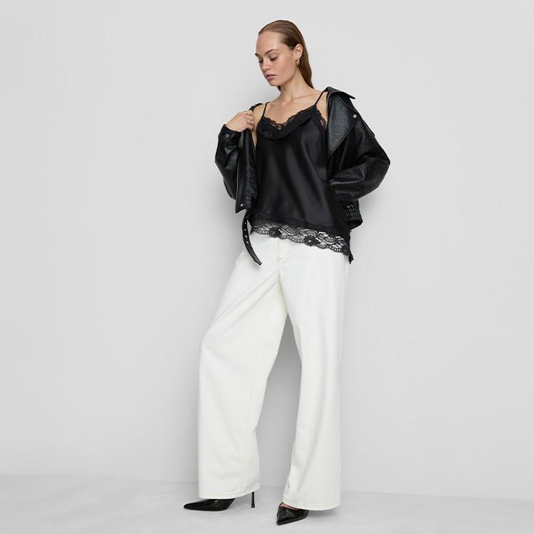 Woman wearing black satin camisole with lace trim, leather jacket and white wide-leg trousers.