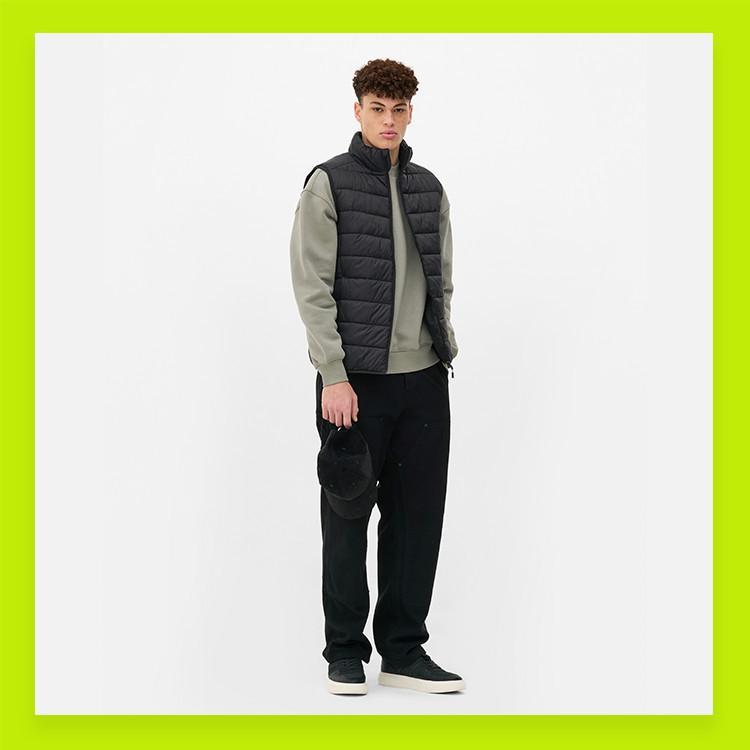 Person wearing black quilted gilet over sage green sweatshirt with black trousers and trainers.