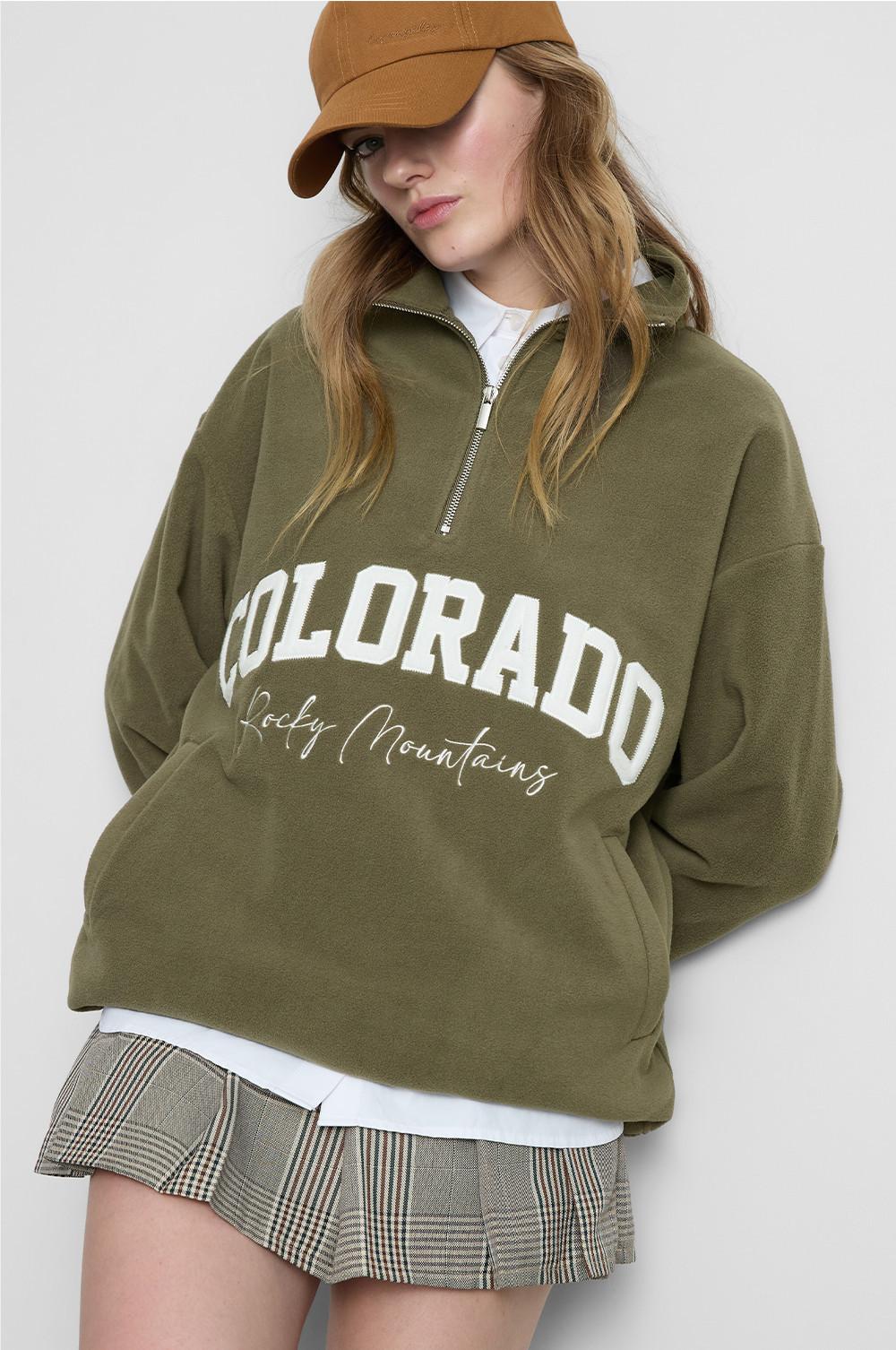Person wearing olive green half-zip sweatshirt with "COLORADO Rocky Mountains" text and a tan cap.