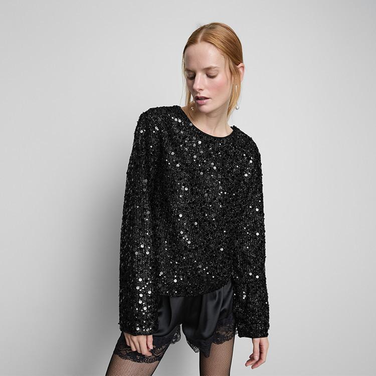 Person wearing a black sequined long-sleeve top with satin shorts featuring lace trim and fishnet tights.