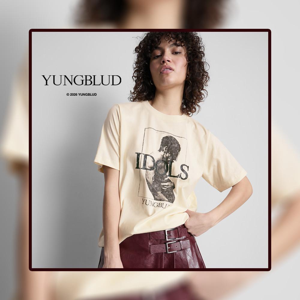 Model wearing cream YUNGBLUD graphic print t-shirt with IDOLS text, paired with burgundy trousers.