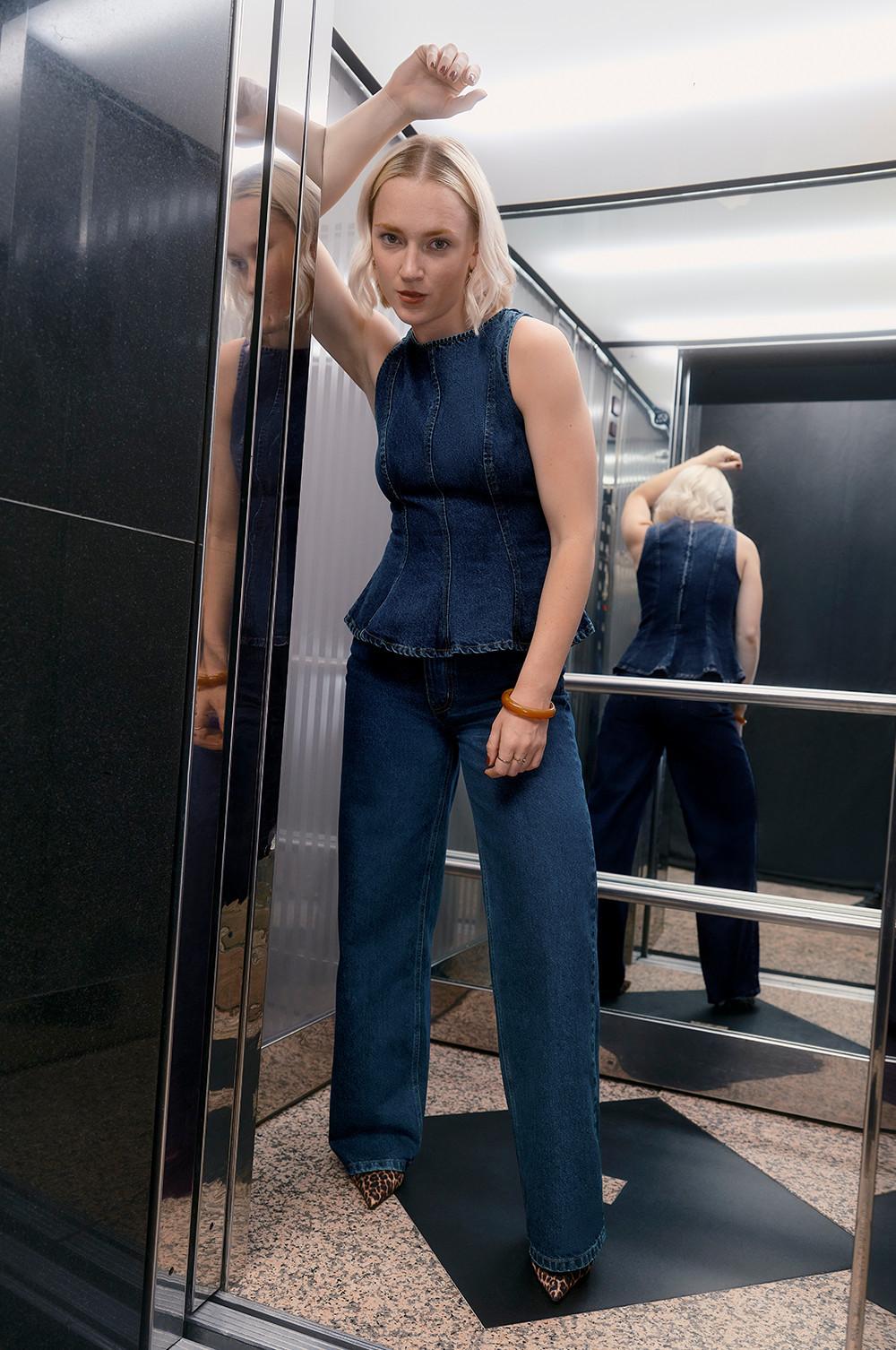 Model v dvigalu, oblečen v peplum top in kavbojke s čevlji z leopardjim potiskom.