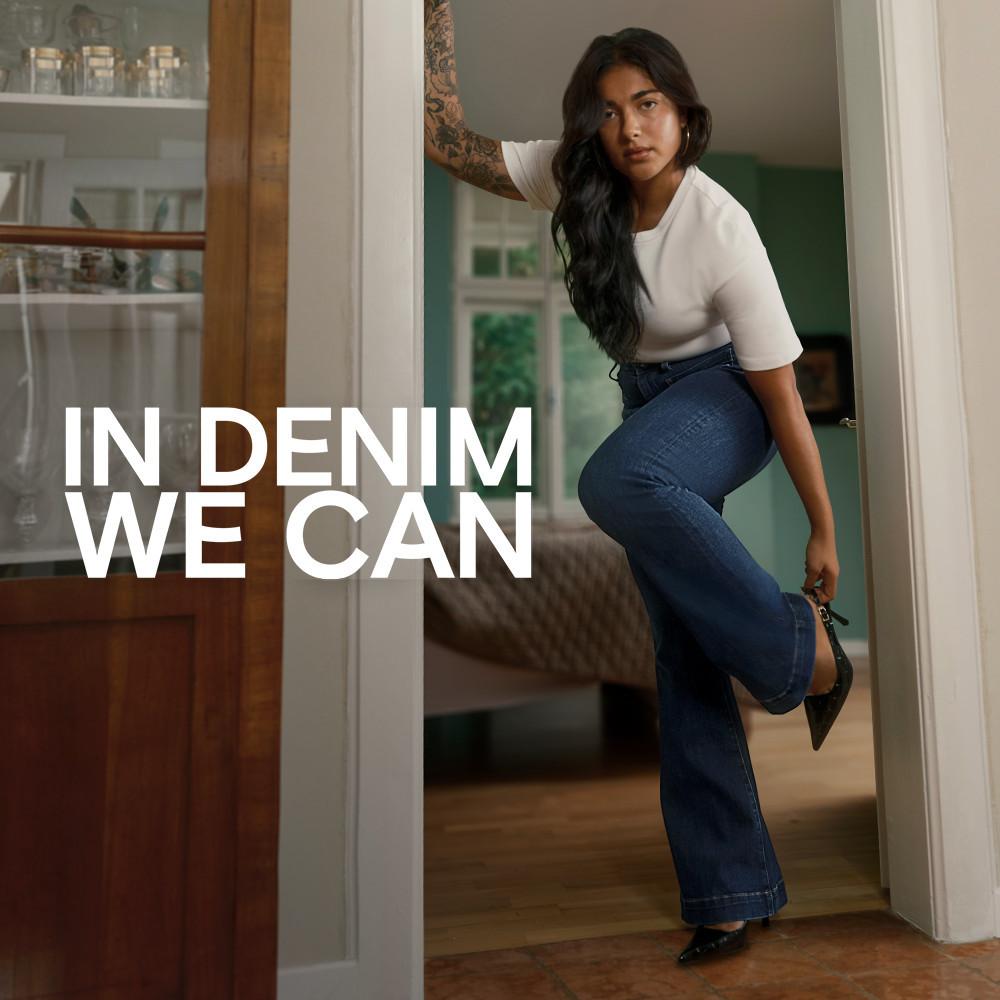 Person wearing white top and blue jeans standing in doorway with text "IN DENIM WE CAN".