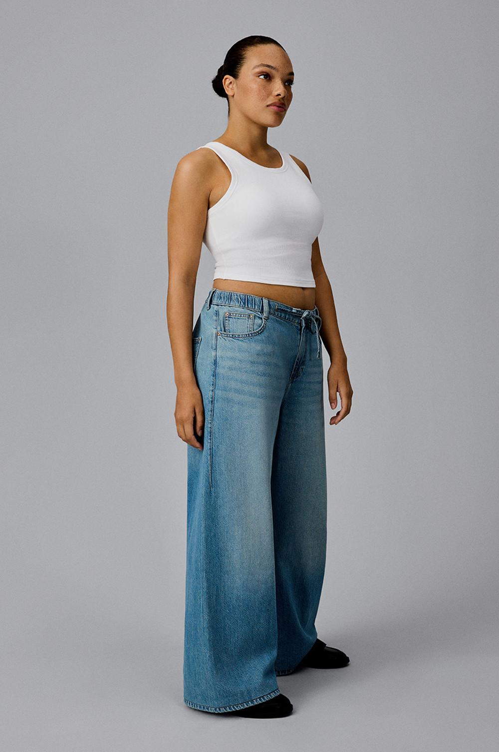 Person wearing white crop top and light blue wide leg jeans with black footwear.