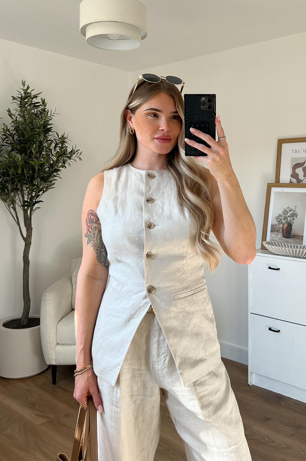 Model wearing cream linen waistcoat with matching cream linen trousers. Paired with a brown bag and sunglasses.