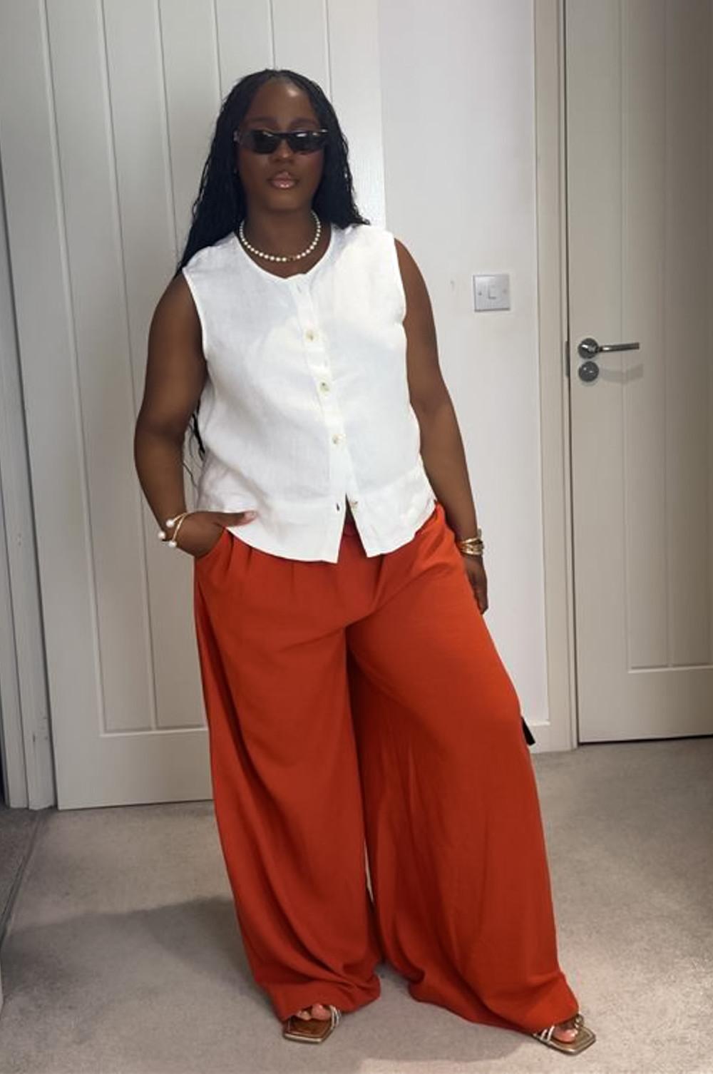 Model wearing wide leg orange linen trousers with a white linen sleeveless top.