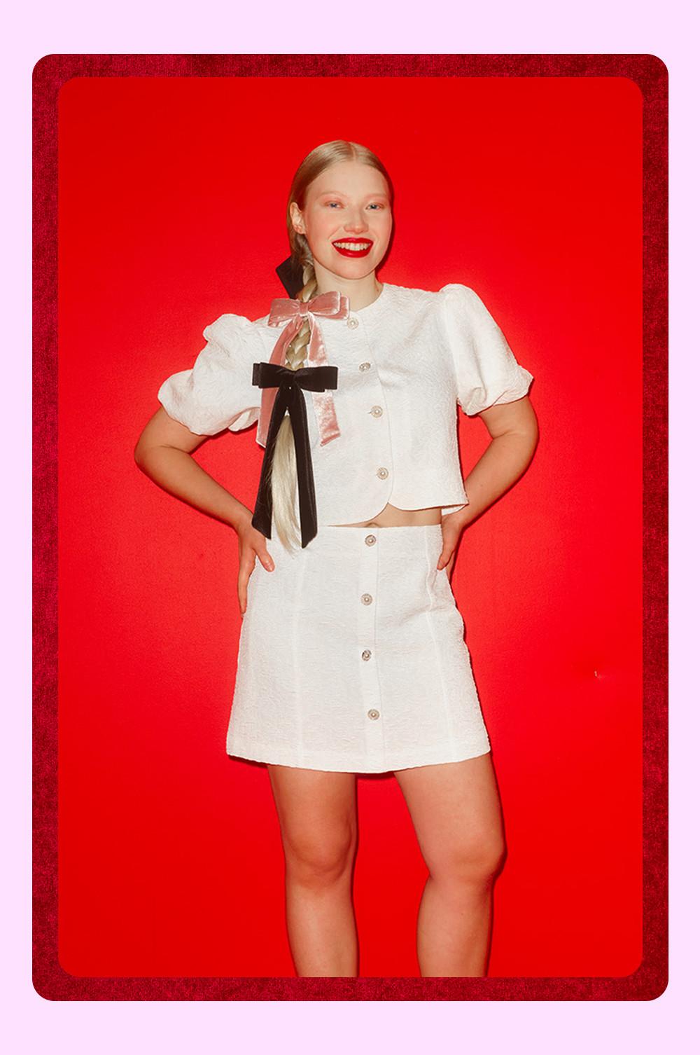 Ensemble deux pièces blanc composé d’un haut court à boutons et d’une mini-jupe assortie ornée de rubans décoratifs.