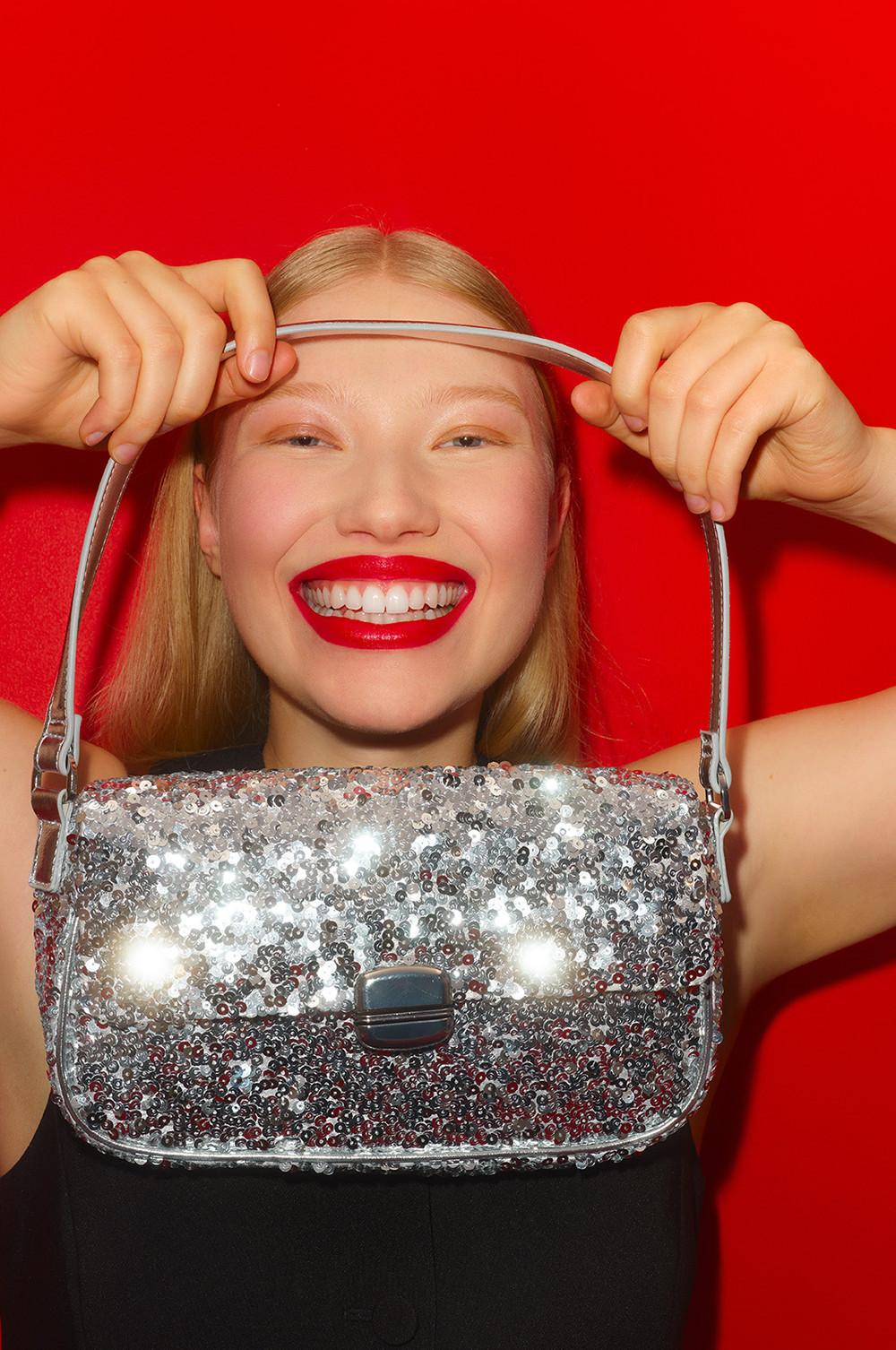 Personne tenant un sac à main argenté étincelant à sequins, devant un fond rouge vif.