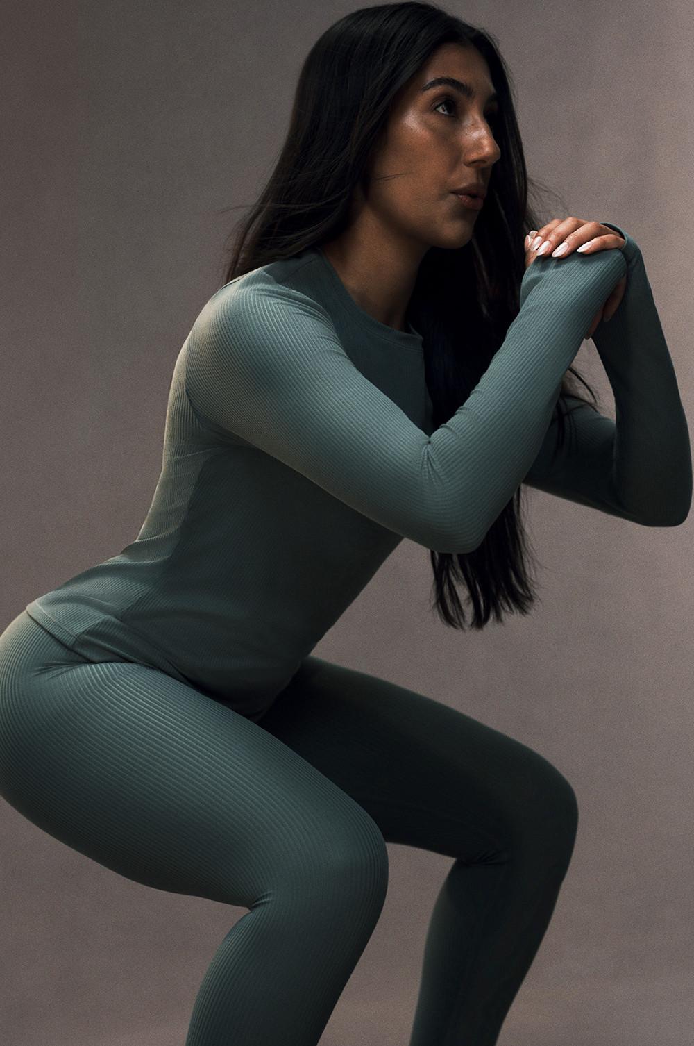 Person in sage green ribbed activewear set in a squat position with long dark hair.