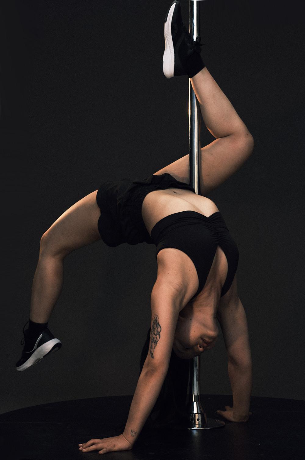 Person performing a pole dance move in black athletic wear and black sneakers with white soles.