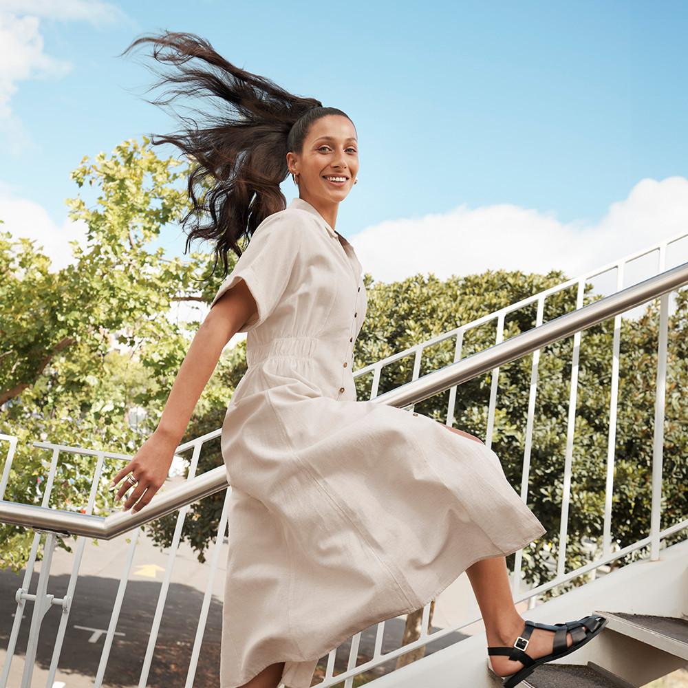Vestido midi com botões à frente com saia esvoaçante e manga curta, usado em escadas exteriores com o cabelo a esvoaçar ao sabor da brisa.