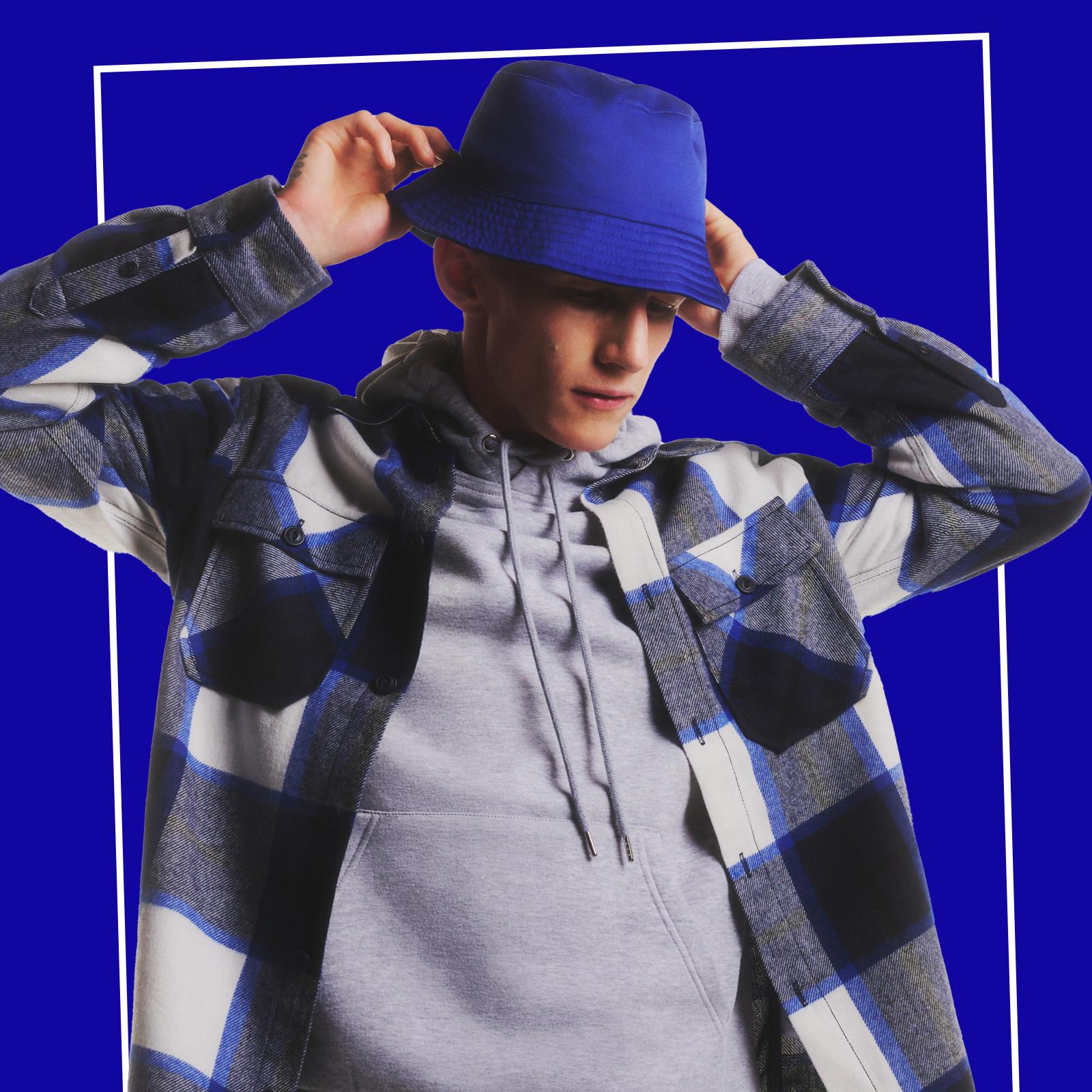 Model wears grey hoodie, shacket and blue bucket hat