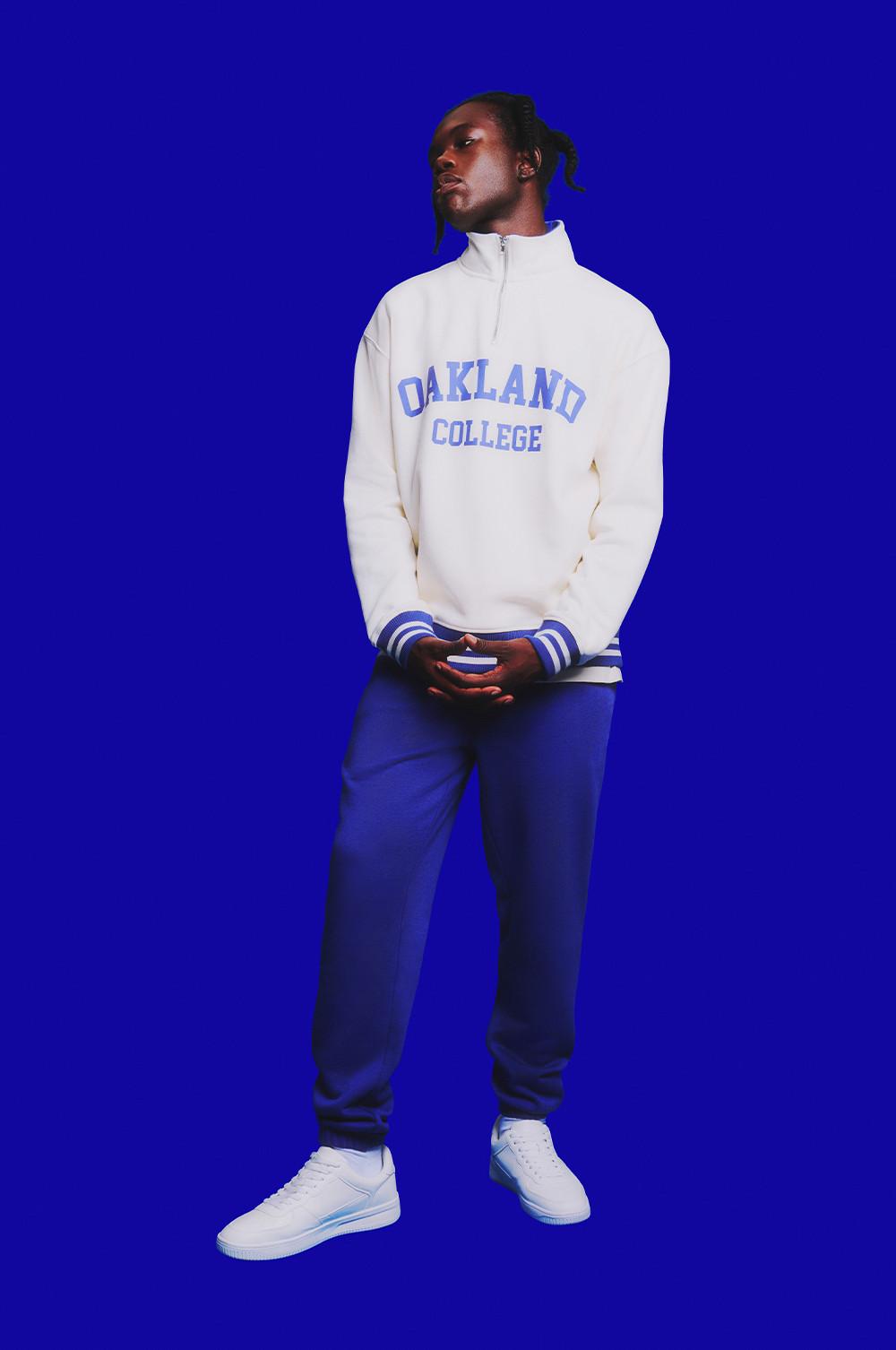 model wears white quarter zip sweatshirt with blue text
