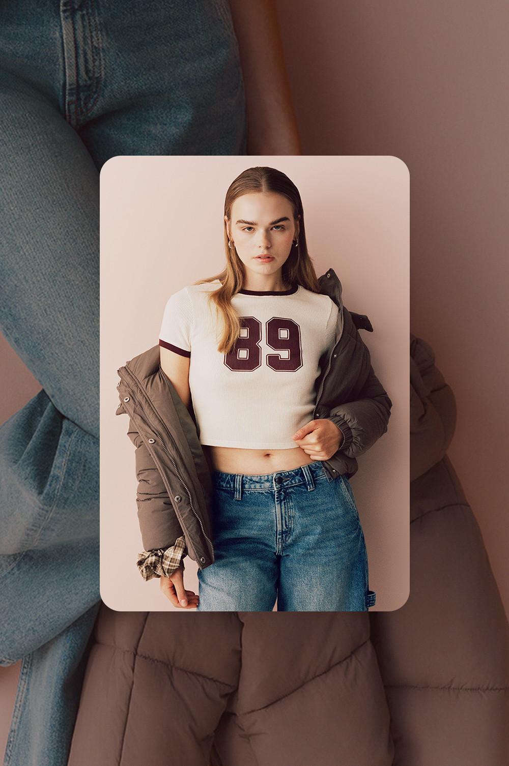 Modella che indossa una maglietta corta bianca con 89 al centro, jeans blu e giacca