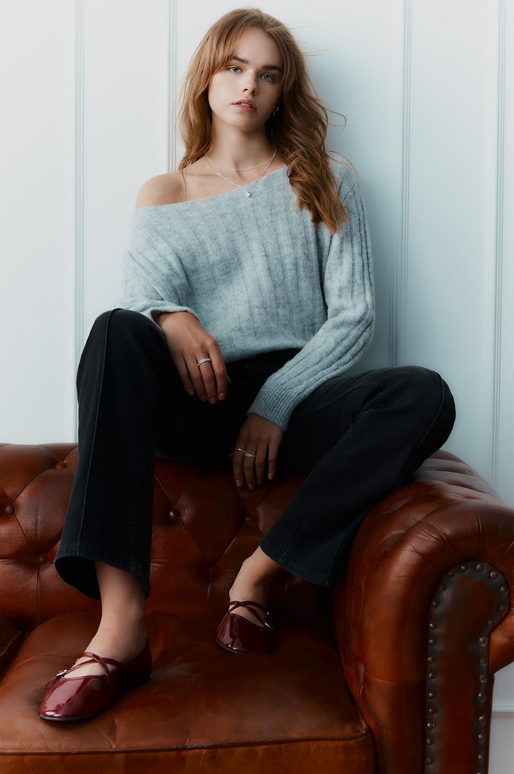 Modella che indossa un maglione con spalle scoperte blu con jeans e ballerine
