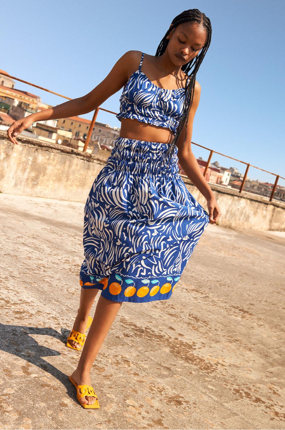 Vrouw in een bijpassende blauwe en witte set met patroon en oranje details en oranje sandalen