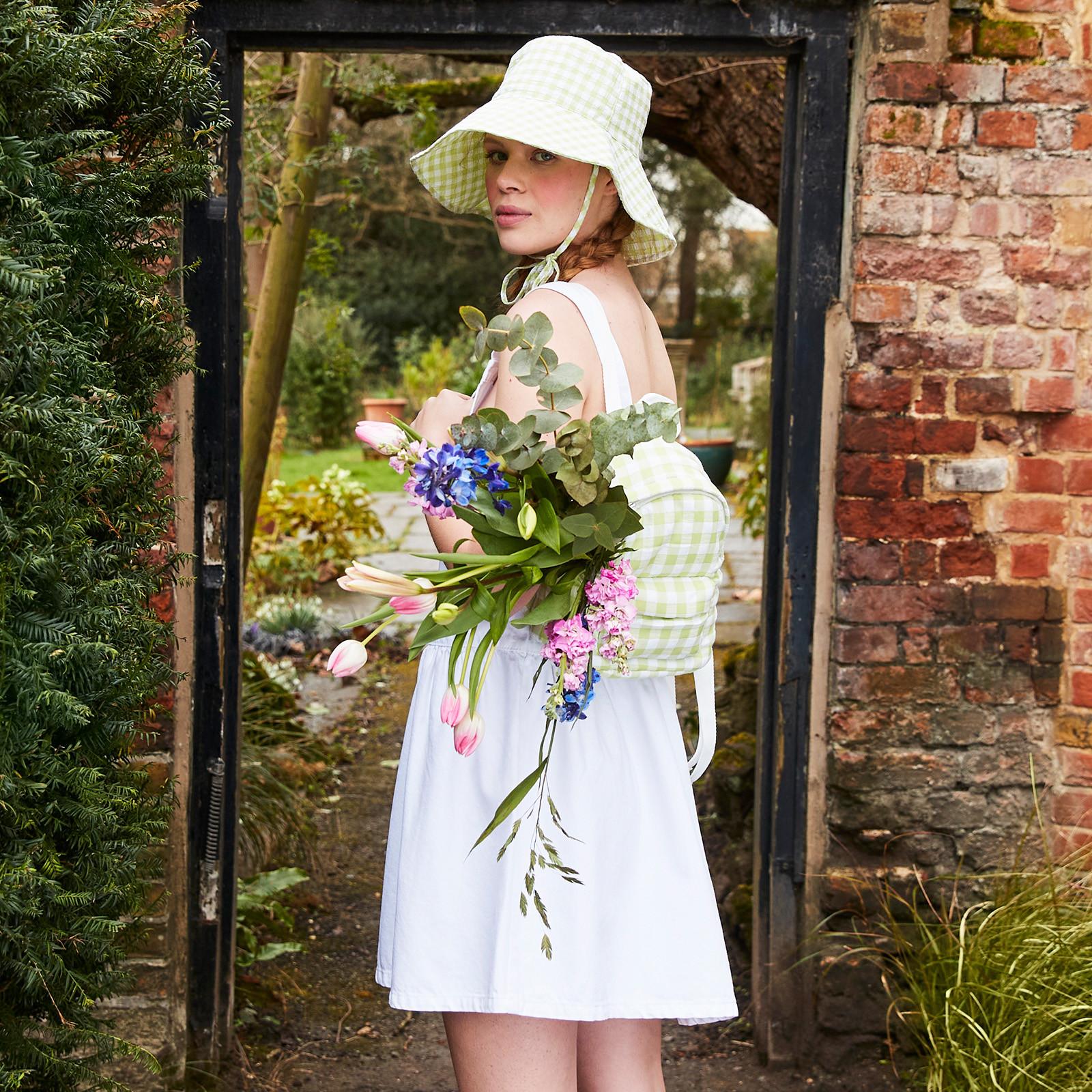 Mannequin portant une robe blanche smockée sans manche avec un sac à dos en vichy et un bob assorti