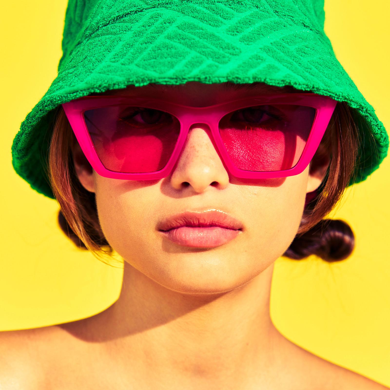 Model wears green bucket hat and pink sunglasses