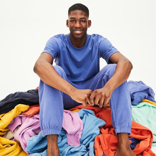 Model wears blue joggers and matching blue top, sitting on a pile of colorful clothes