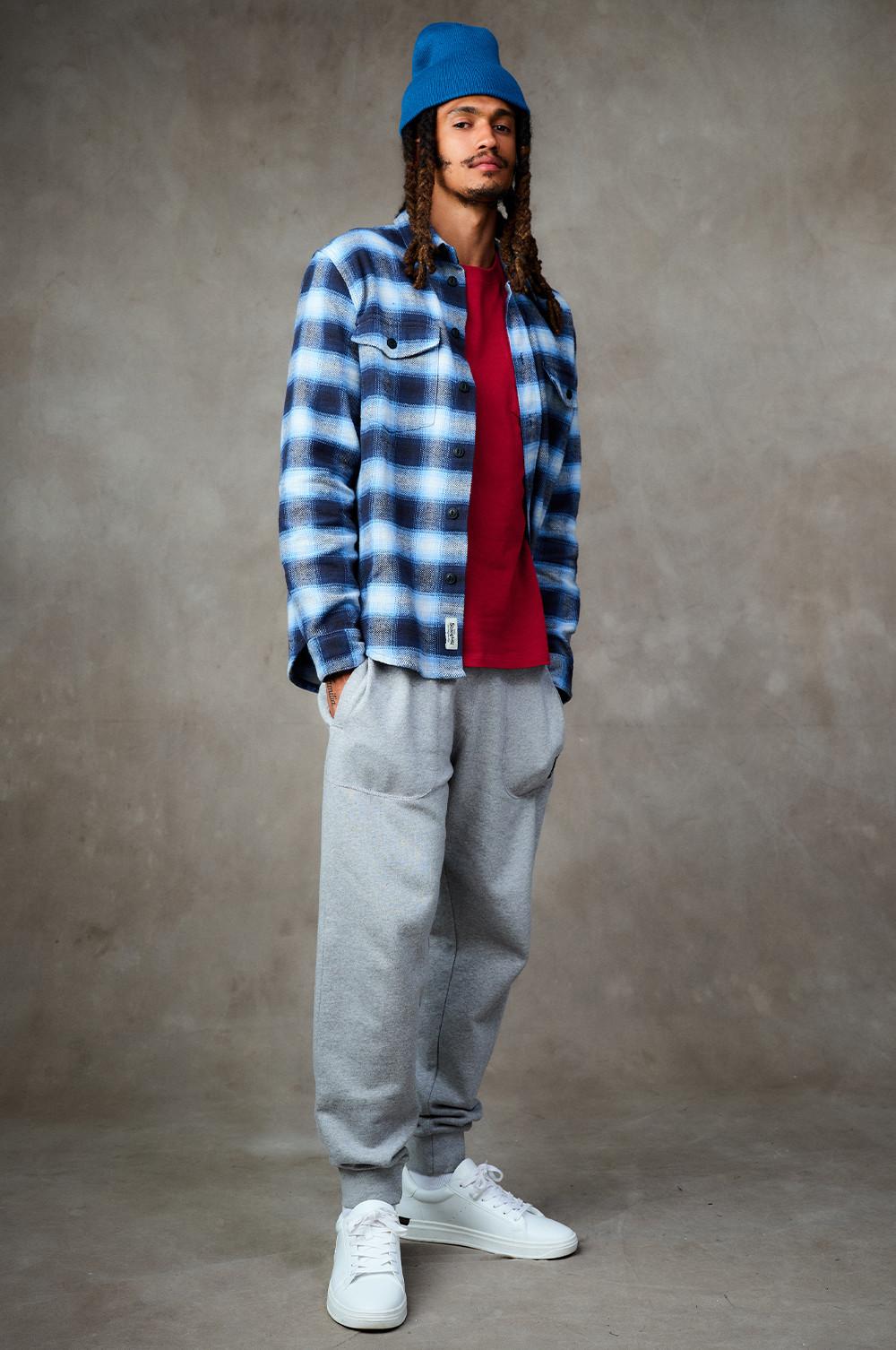 Model wears blue checked shirt, red tshirt, grey joggers and blue beanie