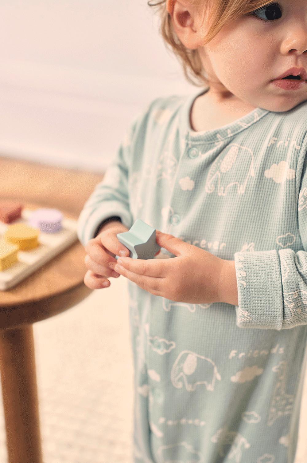 Bébé portant une grenouillère, un jouet en bois à la main