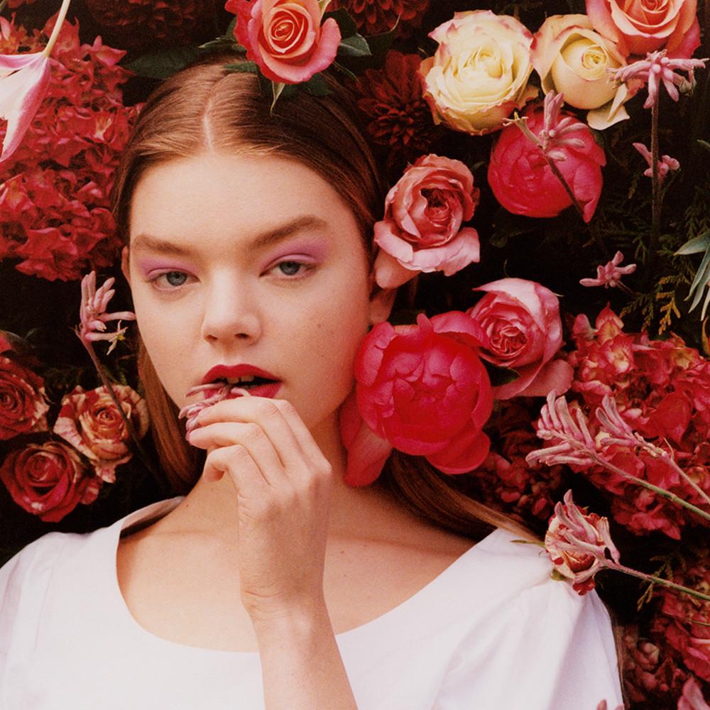 Model trägt rosafarbenes Oberteil mit Puffärmeln vor Blumen-Hintergrund
