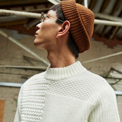 Model looking up, wearing Ivory Cable Knit Sweater, Rust Beanie and glasses