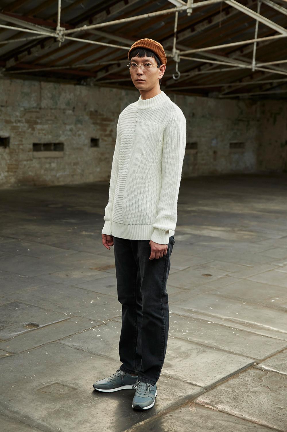 model stands in black twill trousers, ecru knitted jumper and rust coloured beanie, whilst looking a