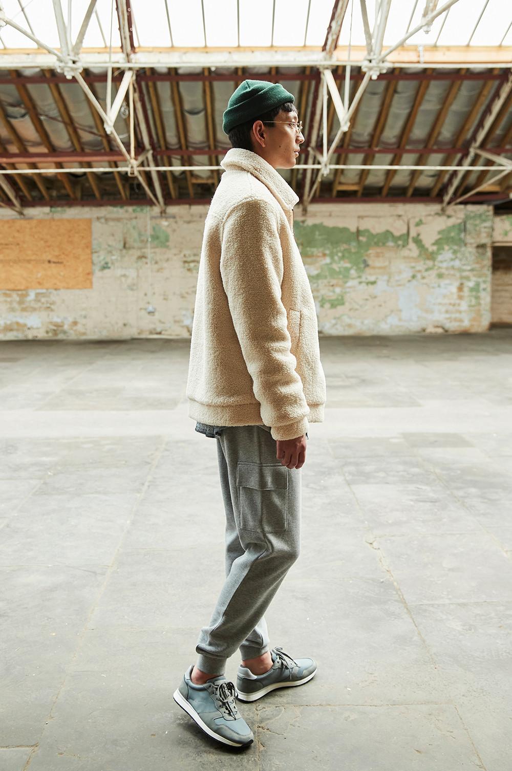 Model wears grey joggers, and borg jacket as he walks away from camera